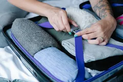 Hands fastening a suitcase strap over folded clothes.