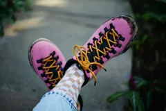 Pink hiking boots with yellow laces and checkered socks being worn outdoors.