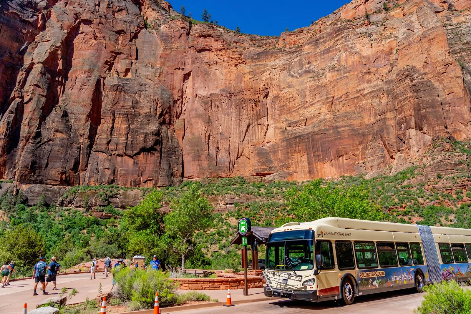 A Zion Canyon electric shuttle at Big Bend with visitors and sandstone cliffs behind it
