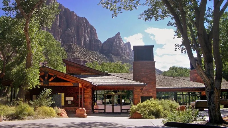 Zion Canyon Visitor Center entrance beneath trees and sandstone cliffs